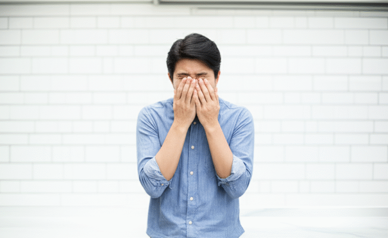 괴로운 듯 두 손으로 코와 눈을 감싸고 있는 남성, 비염으로 인한 불편함을 나타냄